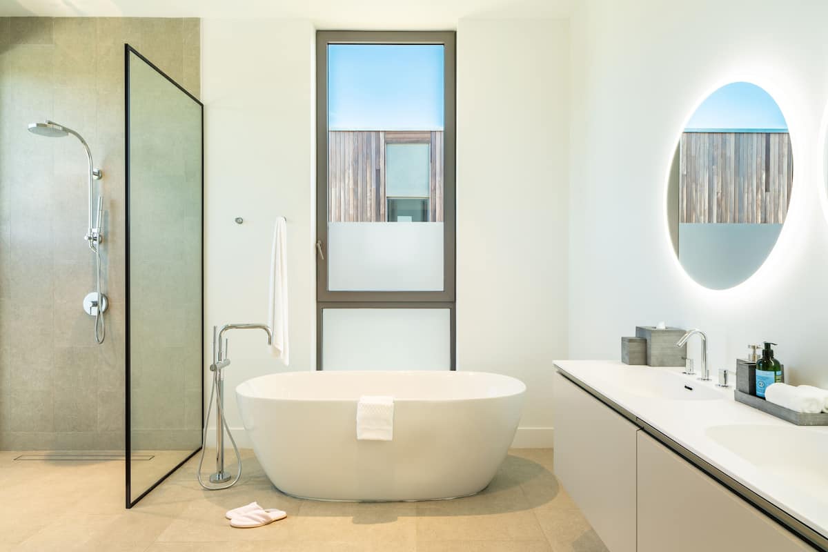 A modern bathroom with a freestanding bathtub, a glass-enclosed shower, and a large mirror with a circular frame.
