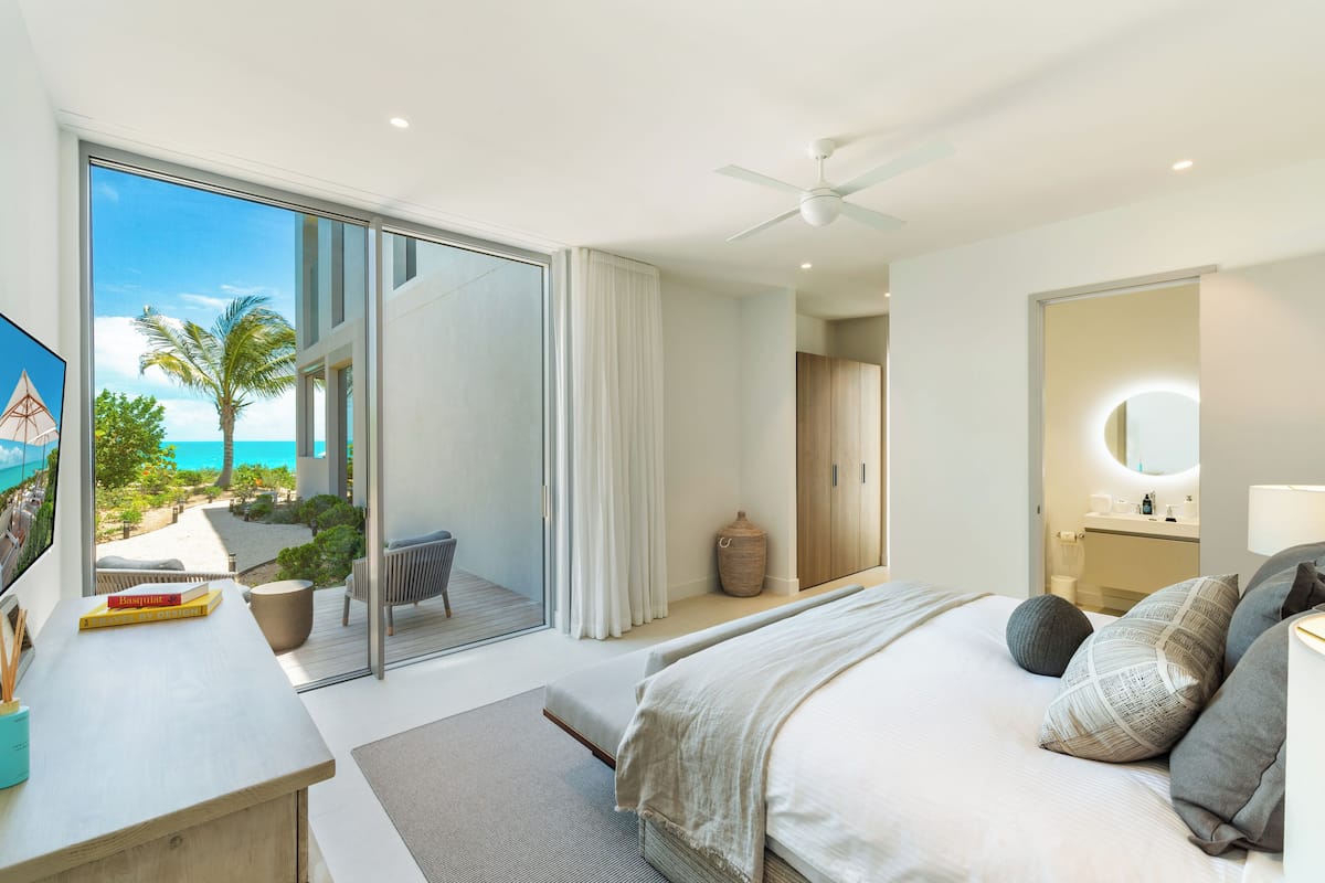 A modern bedroom with a large bed, a desk, and a view of the beach.
