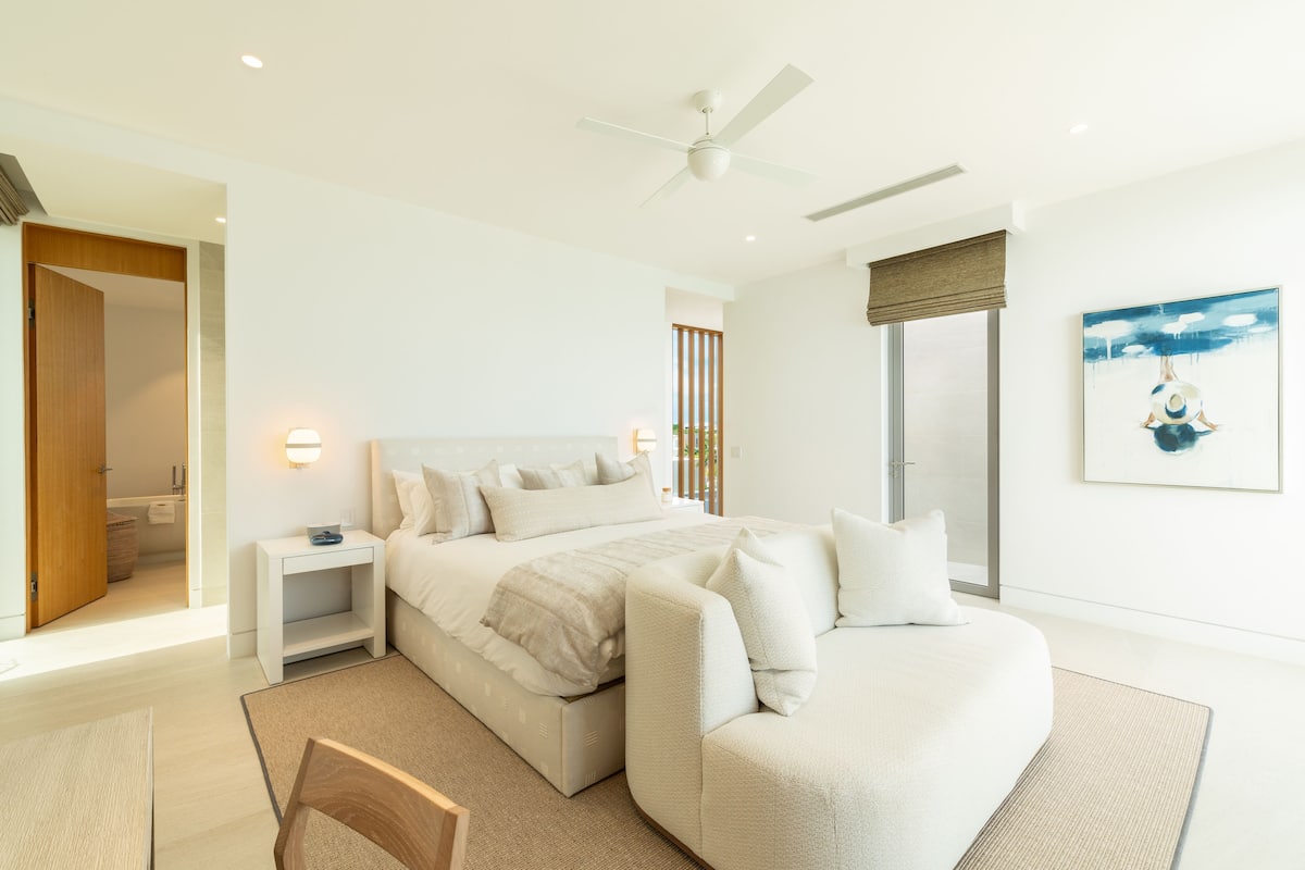 A modern bedroom with a bed, bedside tables, a ceiling fan, and a large window.