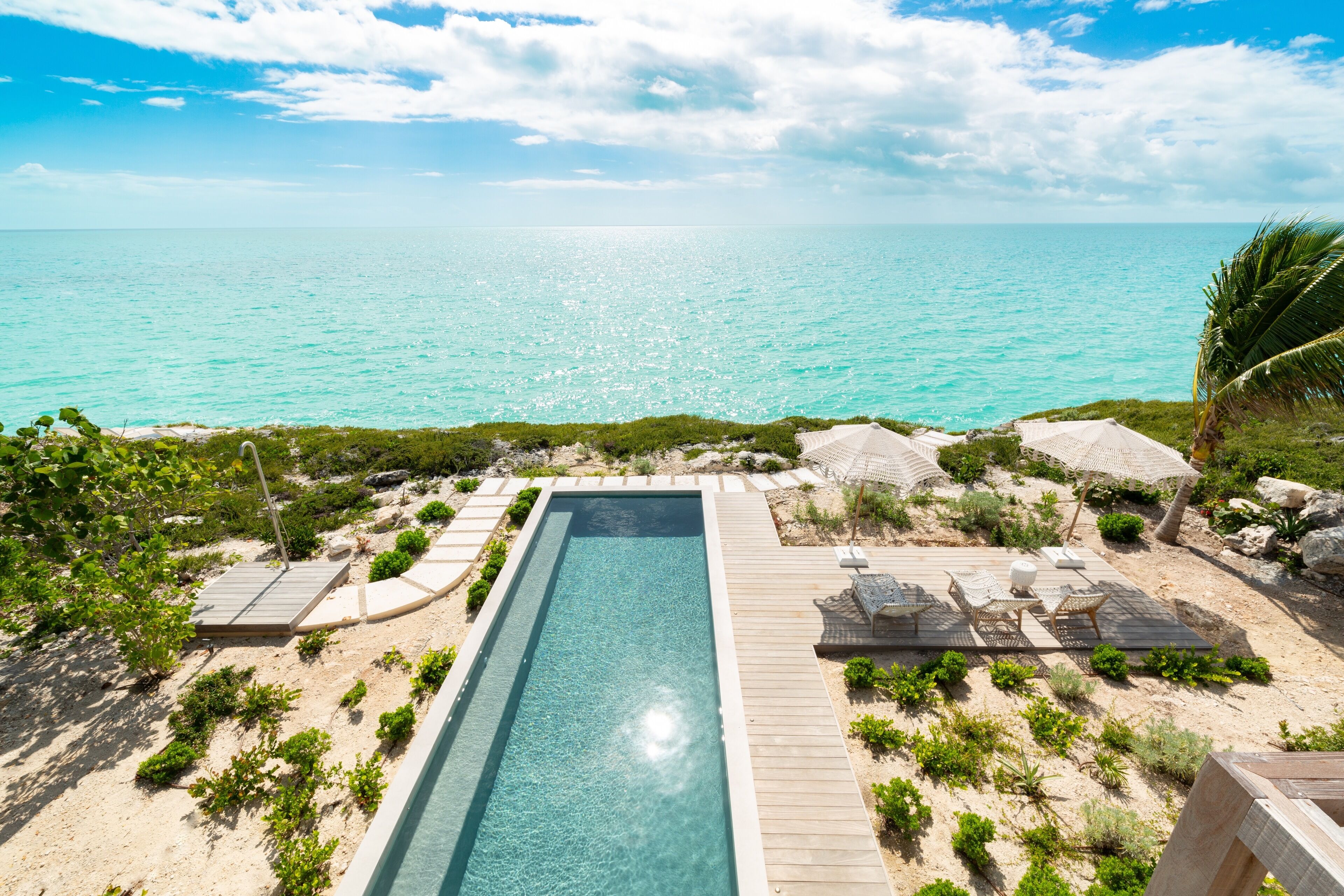 Une piscine rectangulaire entourée d’une terrasse en bois, offrant une vue dégagée sur la plage et l’océan.