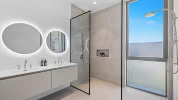 A modern bathroom with a glass shower enclosure, two round mirrors, and a built-in shelf with toiletries.