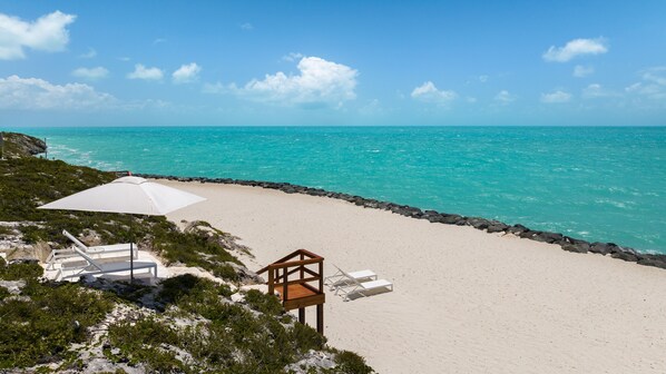 A beach with white sand, a wooden deck, and a white umbrella.