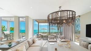 A modern living room with a large window overlooking a pool and ocean, a dining area with a table and chairs, and a comfortable seating area with sofas and a TV. - South Bank (Providenciales)