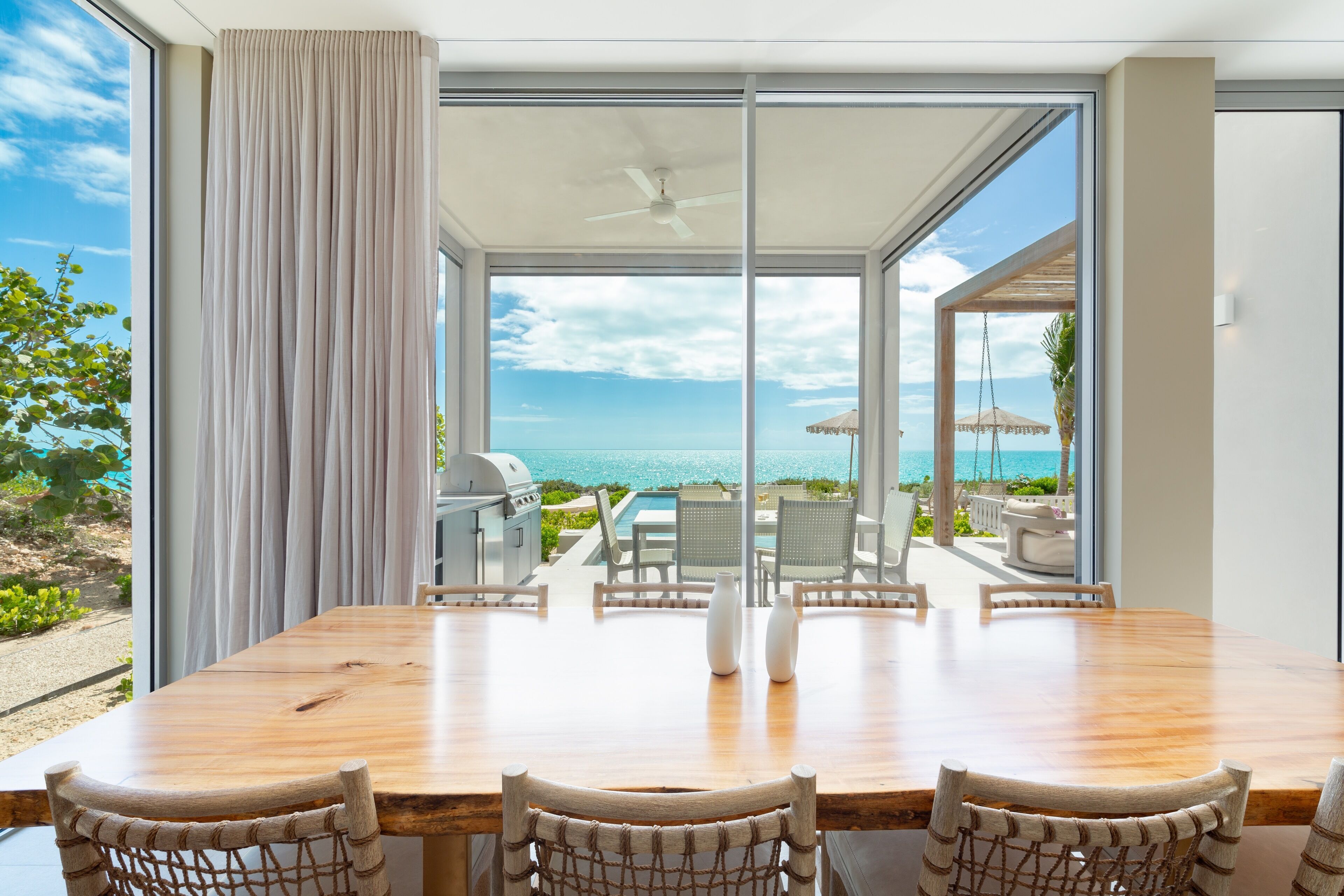 A dining area with a view of the ocean, a ceiling fan, and a grill outside.