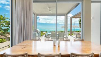 A dining area with a view of the ocean, a ceiling fan, and a grill outside.