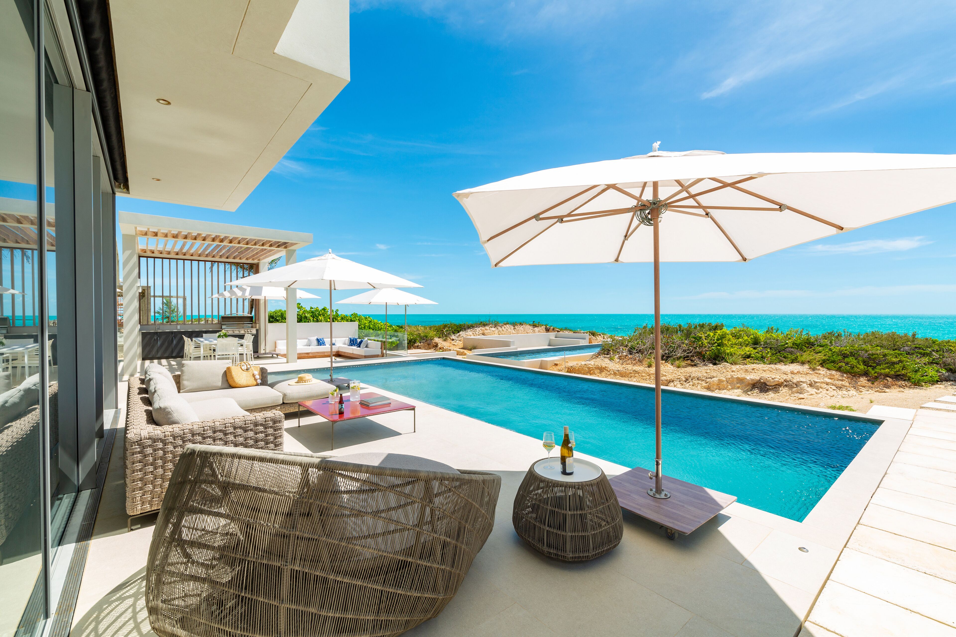 A poolside area with outdoor seating, umbrellas, and a view of the ocean.