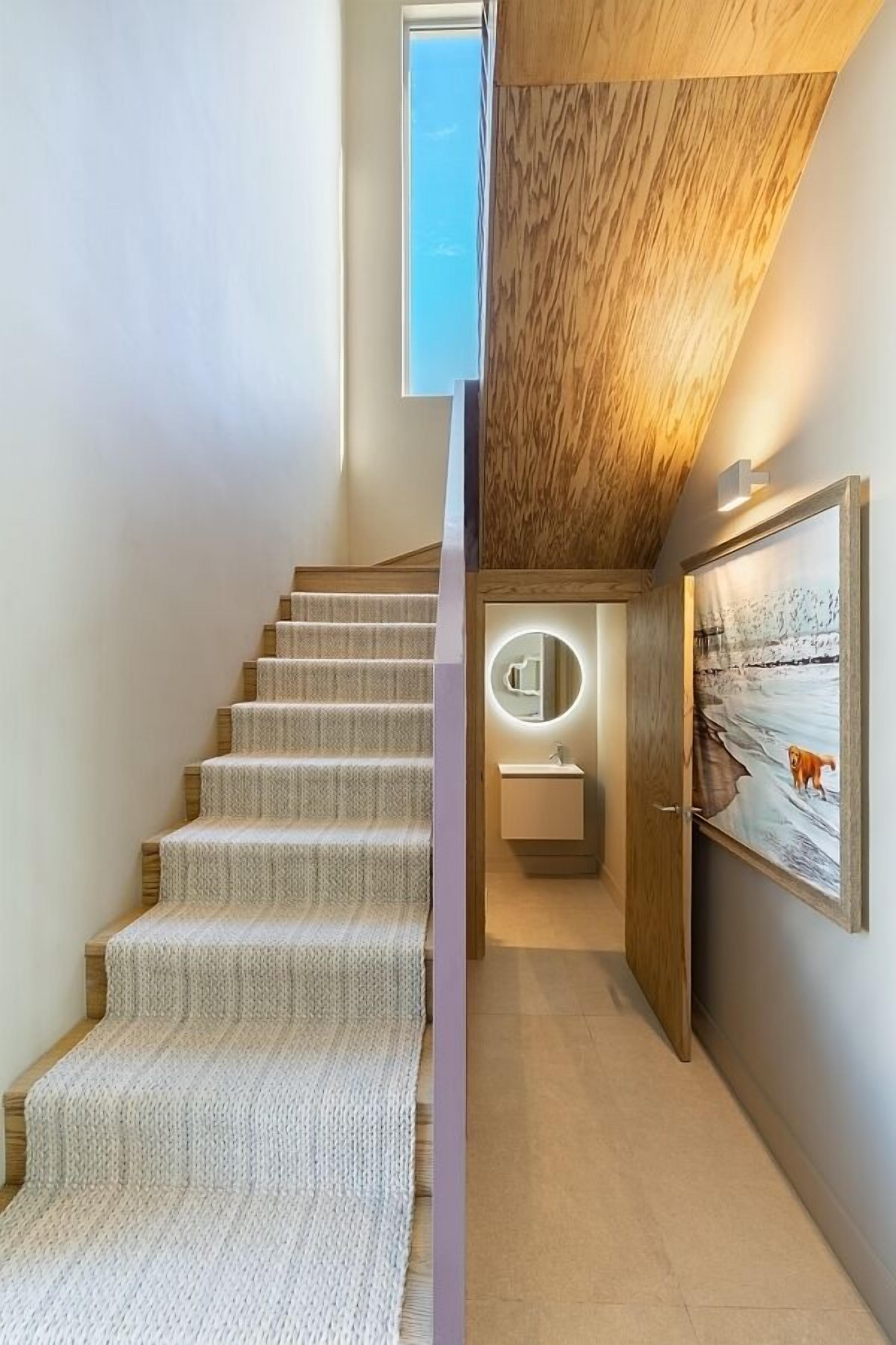 A modern staircase with a textured carpet, a wooden ceiling, and a framed painting on the wall.