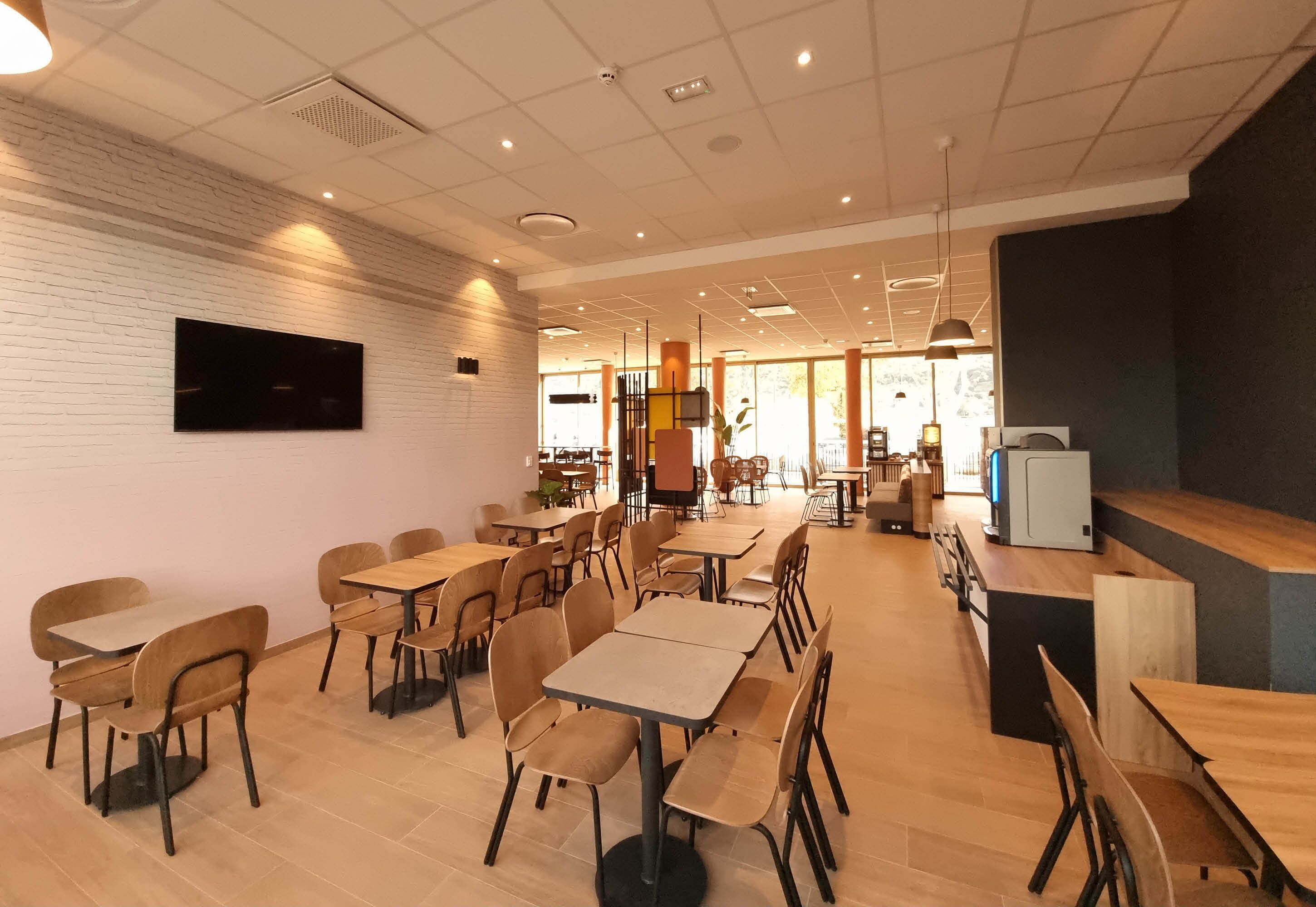 A spacious cafe with multiple tables and chairs, a flat-screen TV mounted on the wall, and a modern interior design.