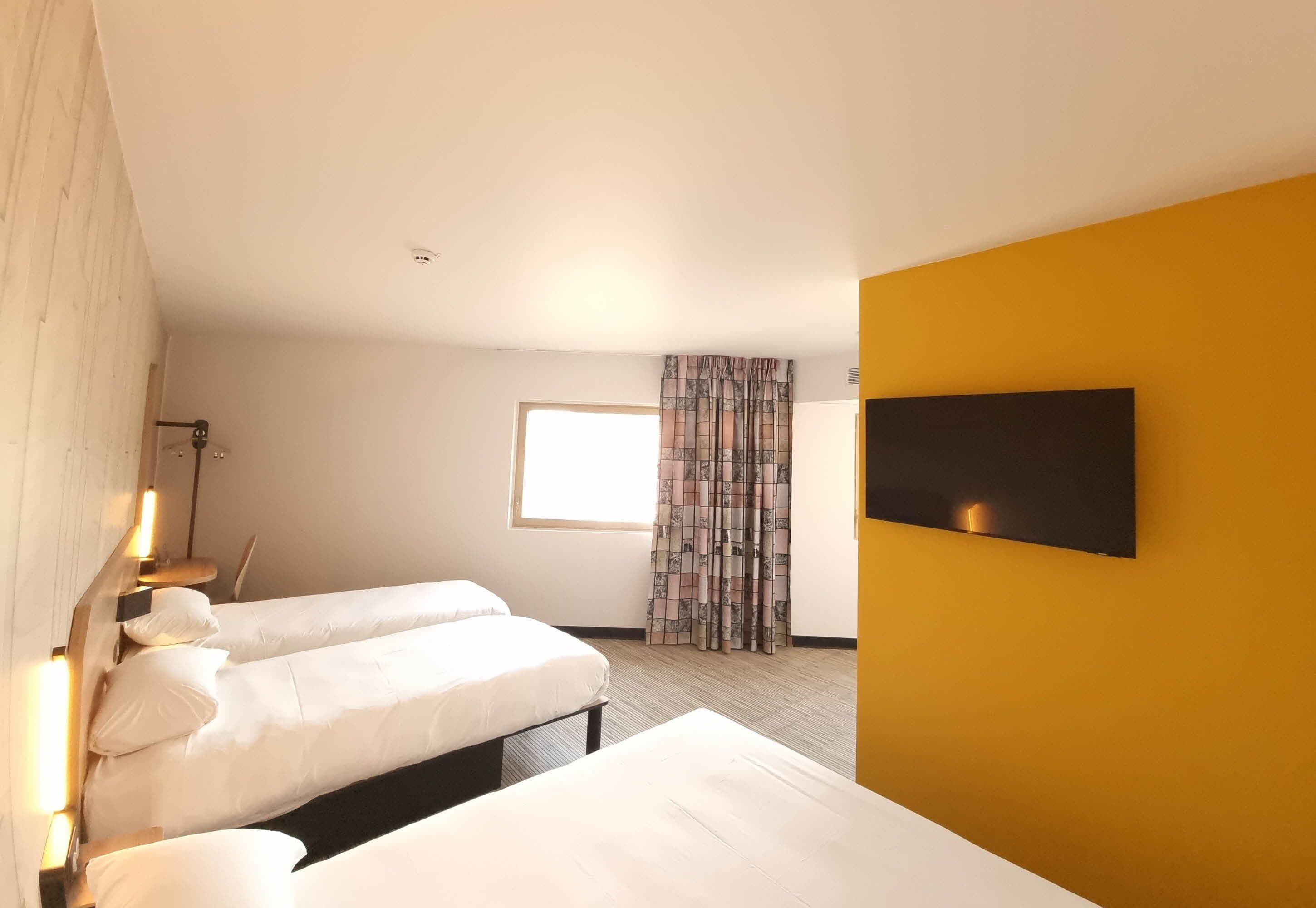 Een hotelkamer met twee bedden, een wandtelevisie en een raam met gordijnen.