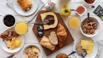 Une table de petit-déjeuner avec divers aliments, notamment des tartines à la confiture, des œufs brouillés, du bacon et des céréales.