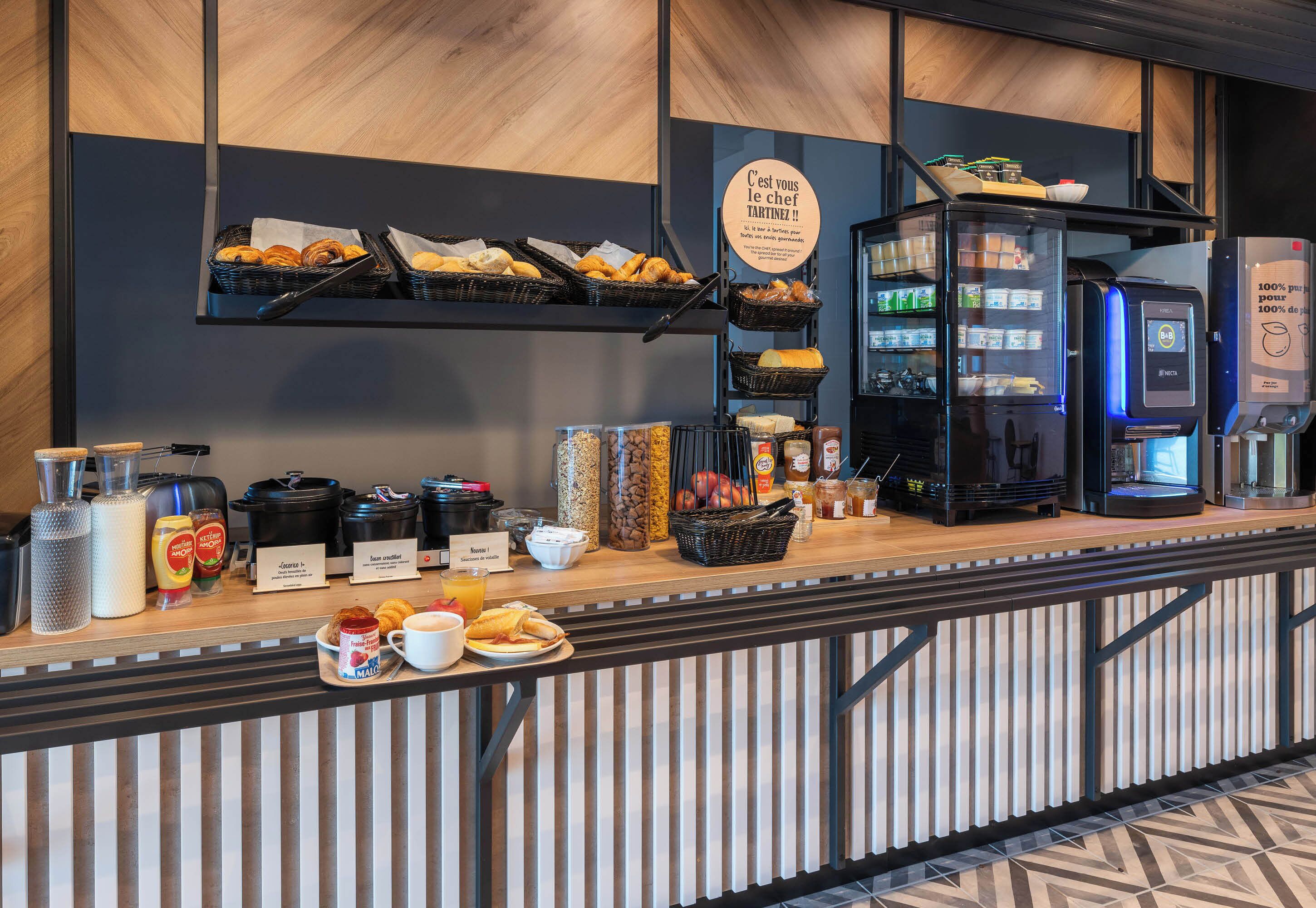 Ein Frühstücksbuffet mit verschiedenen Speisen, einer Kaffeemaschine und einem Kühlschrank.
