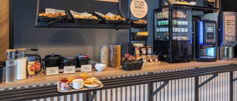 A breakfast bar with various food items, a coffee machine, and a refrigerator.