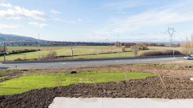 Eine Straße mit einer Grünfläche im Vordergrund und einem entfernten Blick auf eine Stadt und Berge.
