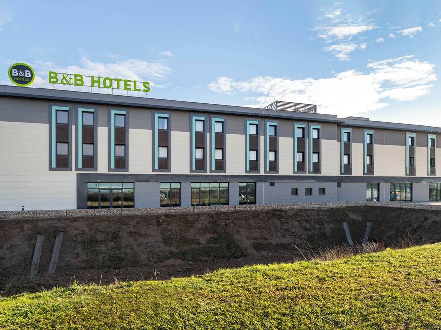 Un moderno edificio de casa de huéspedes con techo plano, amplios ventanales y un área verde al frente.