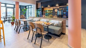 Ein modernes Café mit Sitzgelegenheiten, darunter Tische und eine Bank, einer Kaffeemaschine und einem großen Fenster mit Blick hinaus.