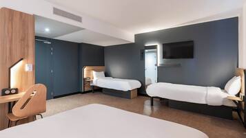 Ein Hotelzimmer mit zwei Einzelbetten, einem Schreibtisch mit Stuhl, einem an der Wand befestigten Fernseher und einer Holzvertäfelung an der linken Wand.