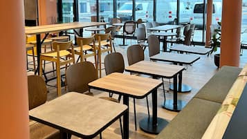 Een modern café met verschillende zithoeken, inclusief tafels en stoelen, en grote ramen met uitzicht op de straat.