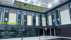 A B&B hotel with a modern facade, large windows, and a clear sky. - B&B HOTEL Massieux Genay (Genay)