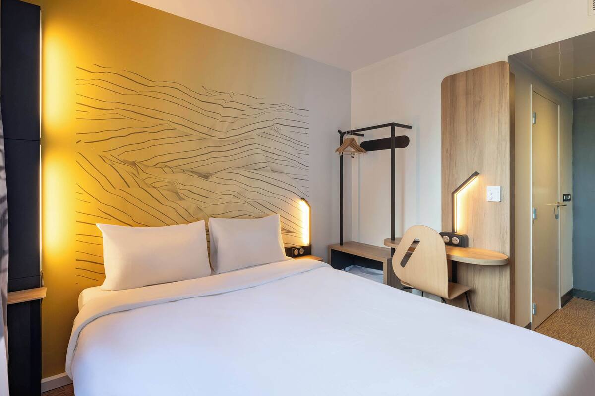 Une chambre d’hôtel moderne équipée d’un grand lit, d’un bureau avec une chaise, d’un porte-manteau et d’une armoire.