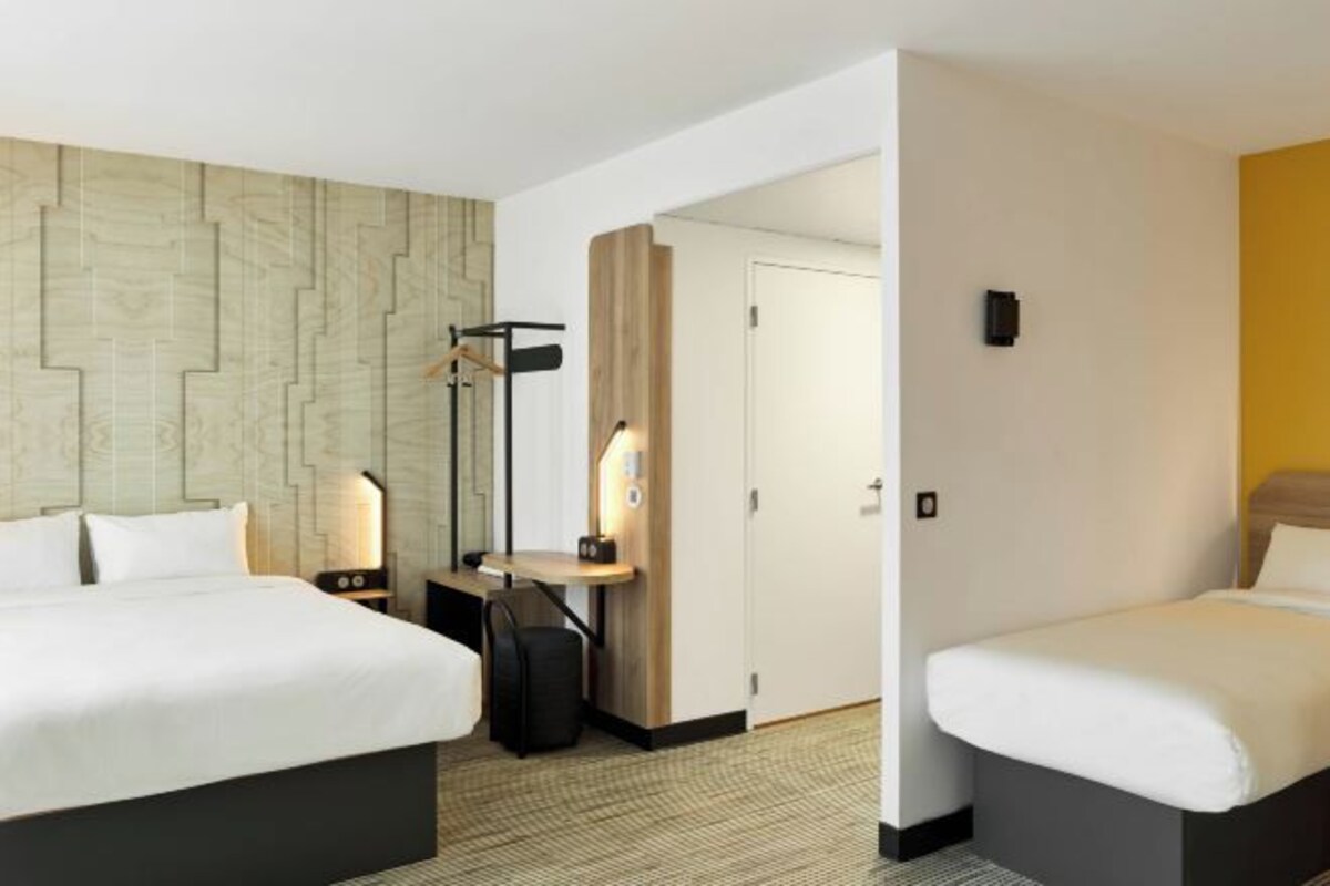 Une chambre d’hôtel avec deux lits, un bureau, une chaise, une lampe et une armoire.