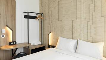 Een hotelkamer met een houten hoofdeinde, nachtkastje met een radio en een hangende kapstok.