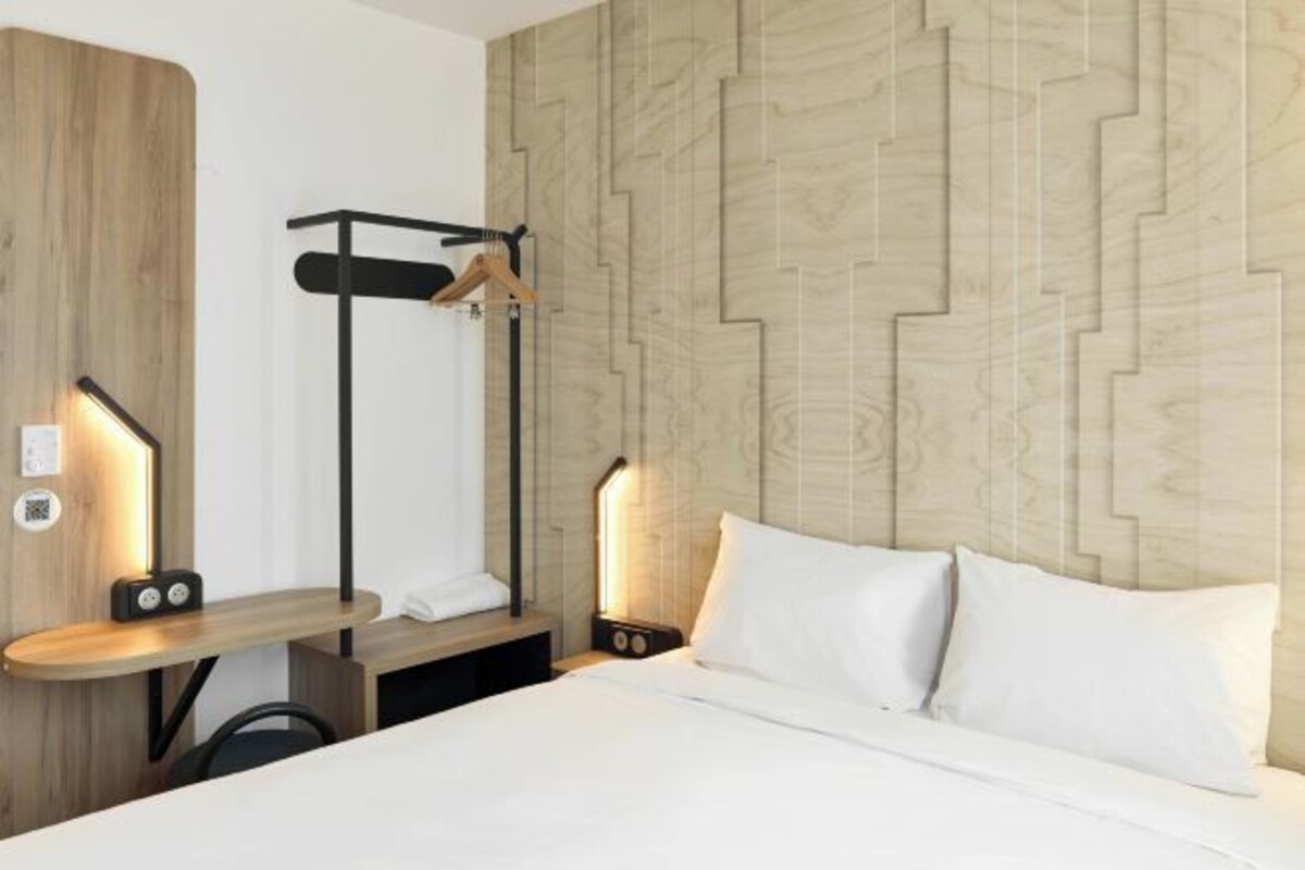 Une chambre d’hôtel moderne équipée d’un lit, de tables de chevet, d’une étagère fixée au mur et d’un porte-vêtements.