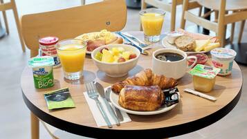 A breakfast table with croissants, fruit, coffee, and juice.