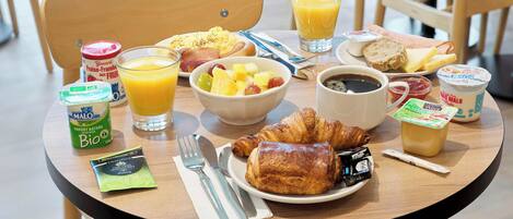 Una mesa de desayuno con cruasanes, fruta, café y jugo.