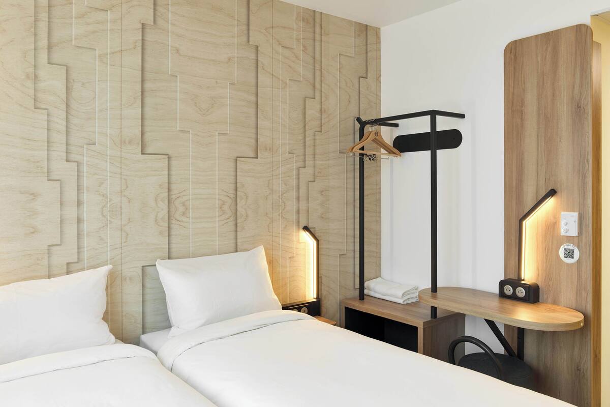 Une chambre d’hôtel avec deux lits, des murs lambrissés, une table de chevet avec une lampe, un porte-manteau et une armoire en bois.