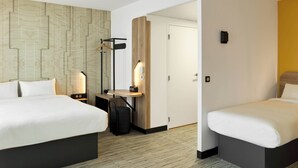 Hotellihuone, jossa on kaksi sänkyä, työpöytä, tuoli, lamppu ja vaatekaappi.