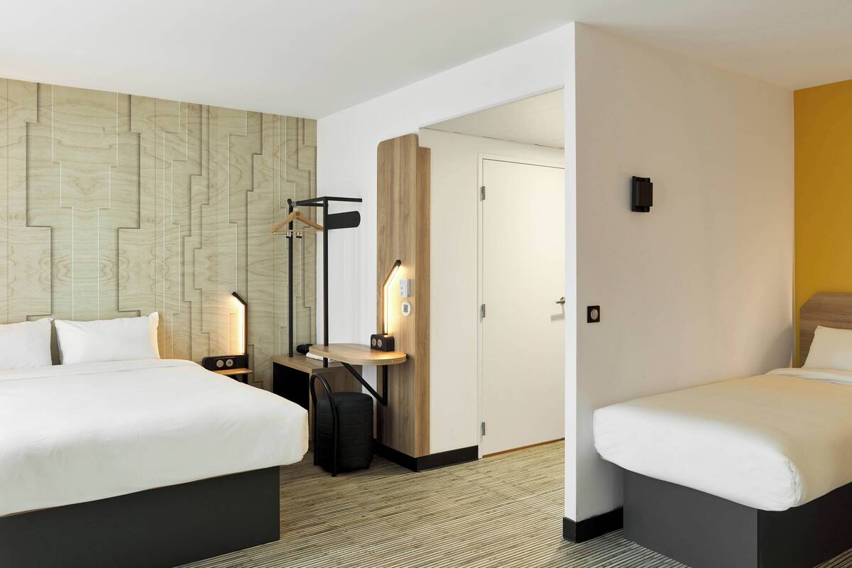 Une chambre d’hôtel avec deux lits, un bureau, une chaise, une lampe et une armoire.