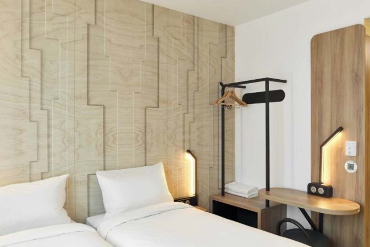 Une chambre d’hôtel moderne avec un mur décoré de panneaux en bois, un lit avec une literie blanche, une table de chevet avec une lampe et un petit bureau avec une chaise.