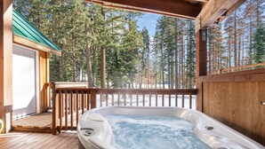 Un jacuzzi en una terraza de madera con vistas a altos pinos.