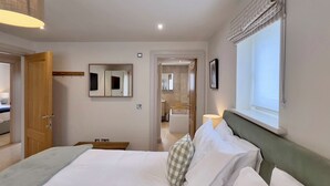 Et hotelværelse med seng, sengebord, lampe, vindue med gardiner og et badeværelse, der kan ses gennem en åben dør.