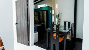 A modern kitchen with a stainless steel refrigerator, a glass dining table with chairs, and a teal accent wall.