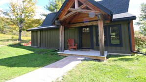 Ein rustikales Blockhaus mit Veranda, einem einzelnen roten Stuhl und einem Weg zum Eingang.