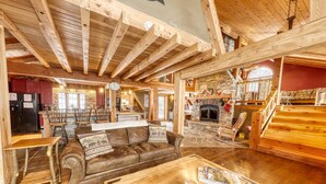 Ein rustikales Lodge-Interieur mit freiliegenden Holzbalken, einem Kamin aus Stein, einem Ledersofa und einer Essecke mit Holztischen und -stühlen.
