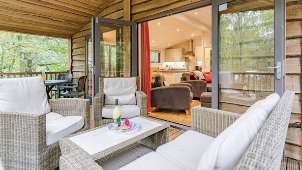 Een houten chalet met rieten meubilair, een eethoek en een keuken zichtbaar door glazen deuren.