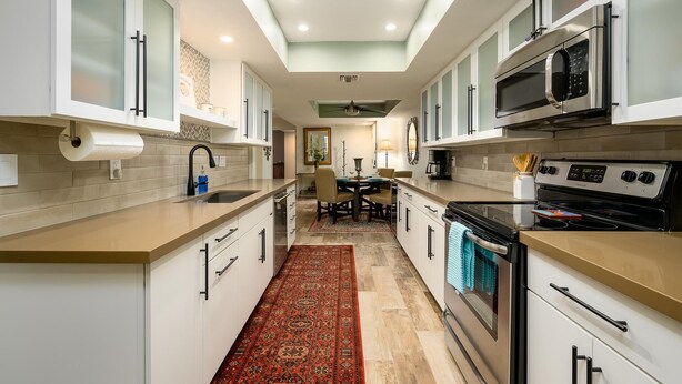 Une cuisine moderne avec des meubles blancs, un îlot central, un four à micro-ondes, un four traditionnel et un coin repas comprenant une table et des chaises.