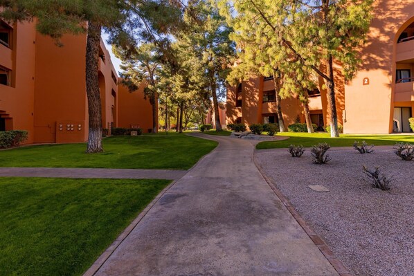 A pathway leading to a building with a uniform exterior and multiple windows. - CASA MERLOT - 1st floor condo near pool, Anasazi Village. (Phoenix)