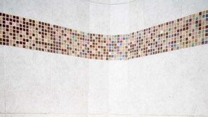 A white toilet with a closed seat, a shower hose, and a tiled wall with a mosaic border. - Korongoro Hotel Chemolingot (Chemolingot)