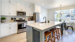Una cocina moderna con armarios blancos, electrodomésticos de acero inoxidable y una isla grande con taburetes de bar.
