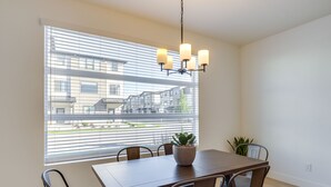 Comedor con mesa, sillas, una araña de cristal y vistas de edificios a través de amplios ventanales.