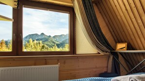 Una habitación con cama, ventana con vistas a la montaña, radiador y paredes de madera.