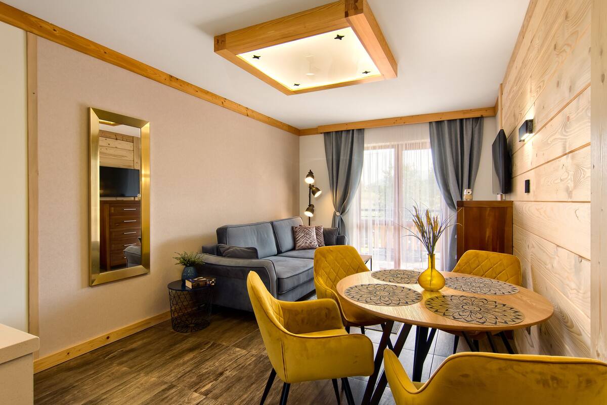 A cozy living room with a sofa, yellow chairs, a round table, and a ceiling light fixture.
