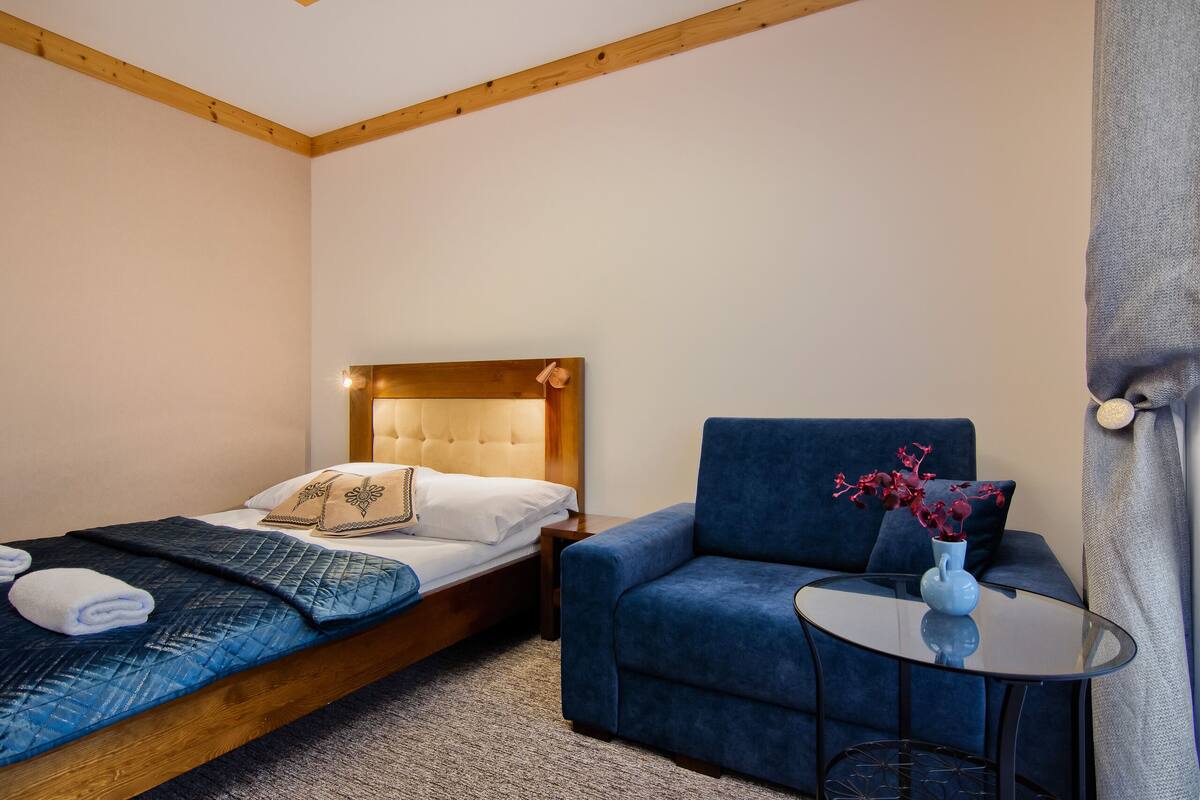A bedroom with a bed, a blue armchair, a small round table, and a vase with flowers.