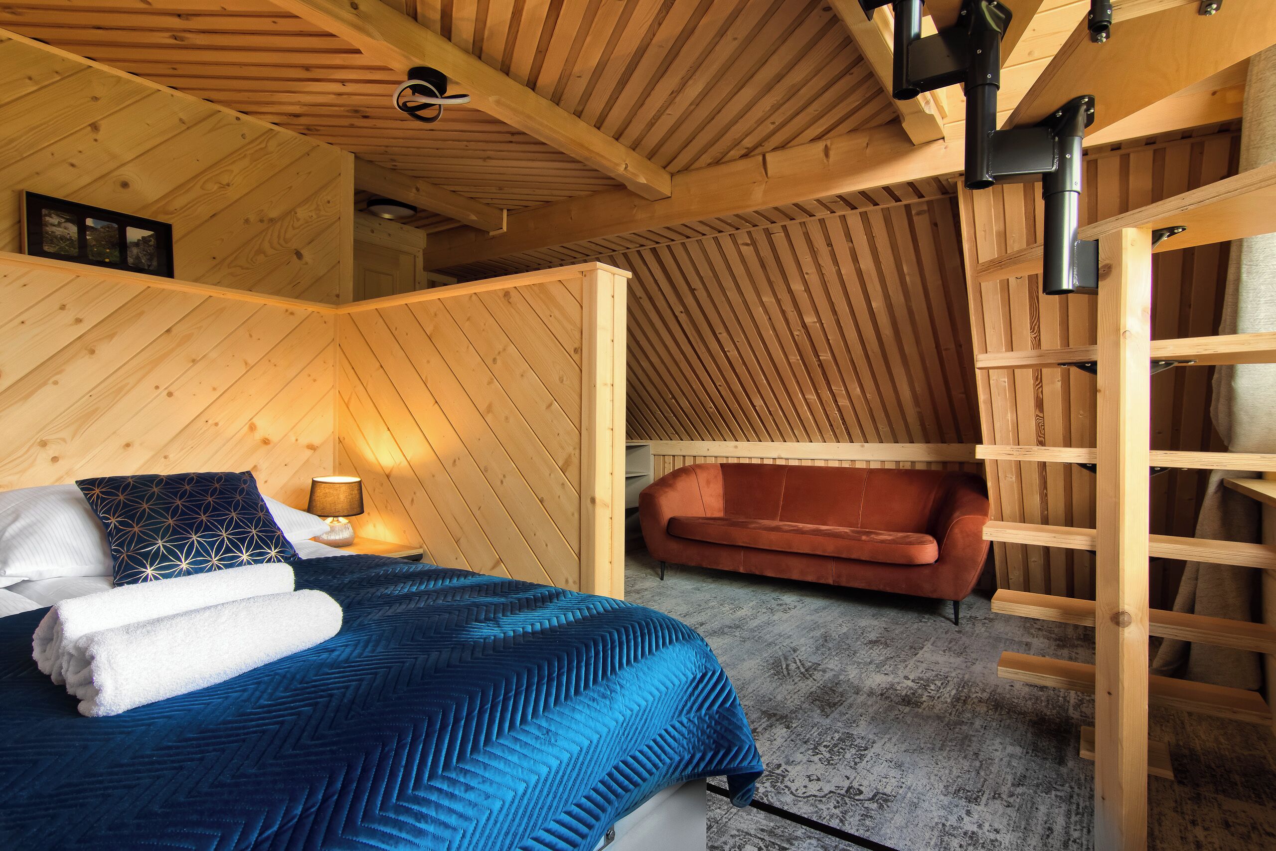 Une pièce chaleureuse avec un lit, un plafond en bois, un canapé rouge et une échelle en bois.