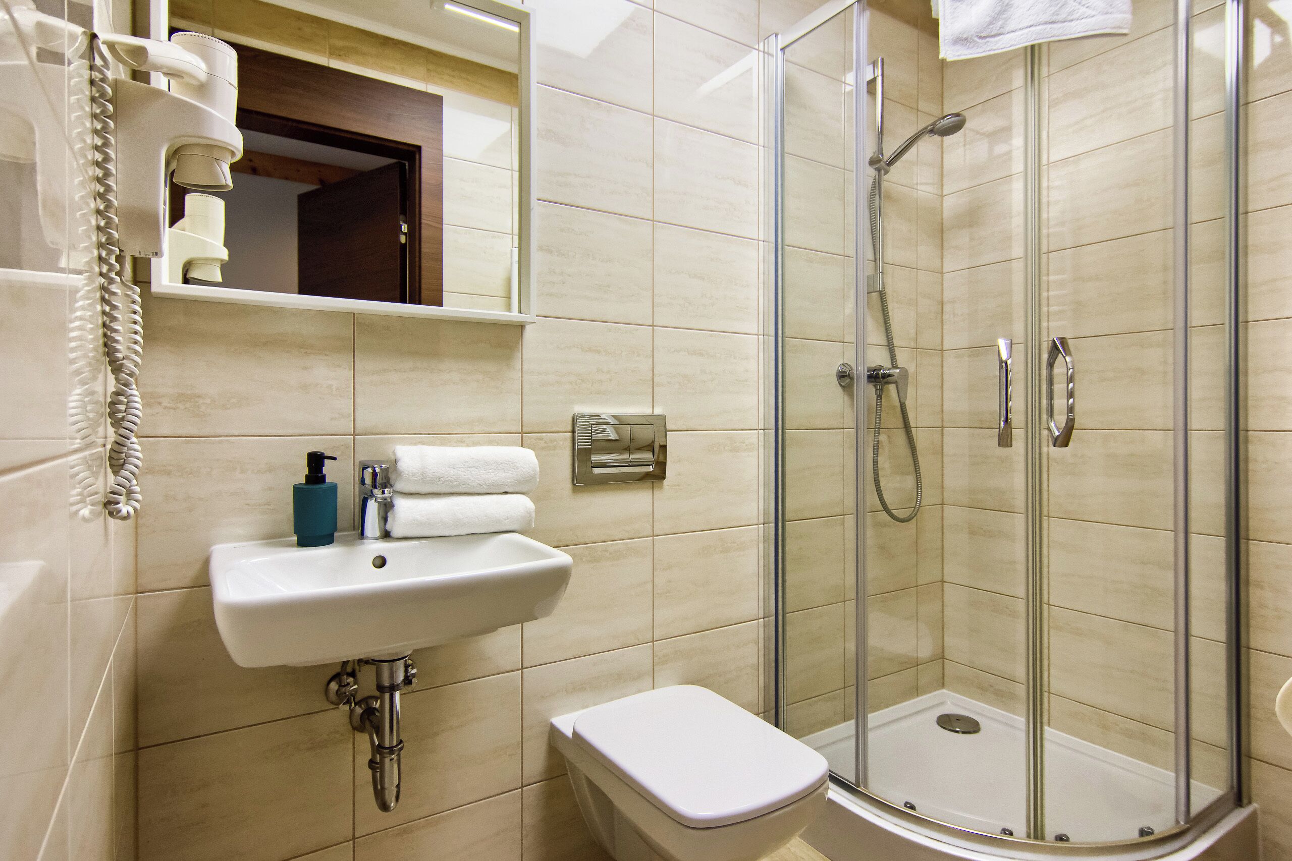 Un baño moderno con ducha envuelta en vidrio, un lavamanos con dispensador de jabón y un inodoro.