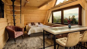 Un dormitorio acogedor con cama, escritorio y sillas, una ventana con vistas a montañas y un techo de madera.