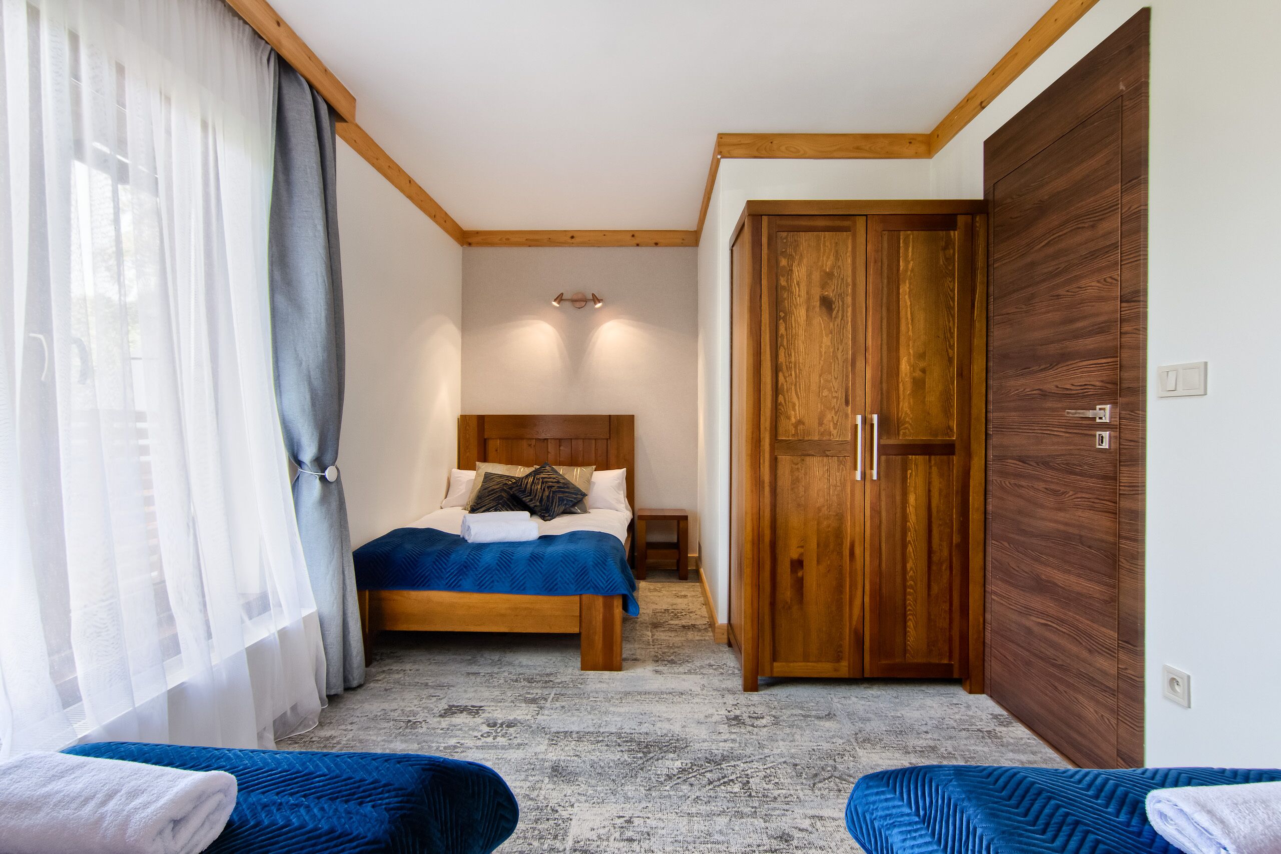 A bedroom with a bed, wooden wardrobe, and a small bedside table.